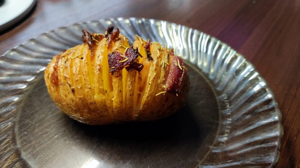 Pieczony ziemniak hasselback z boczkiem i rozmarynem na talerzu.