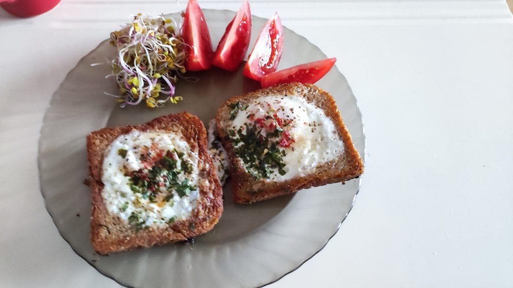 Smażone jajka w tostach, ćwiartki pomidorów i garść kiełków rzodkiewki leżą na talerzu.