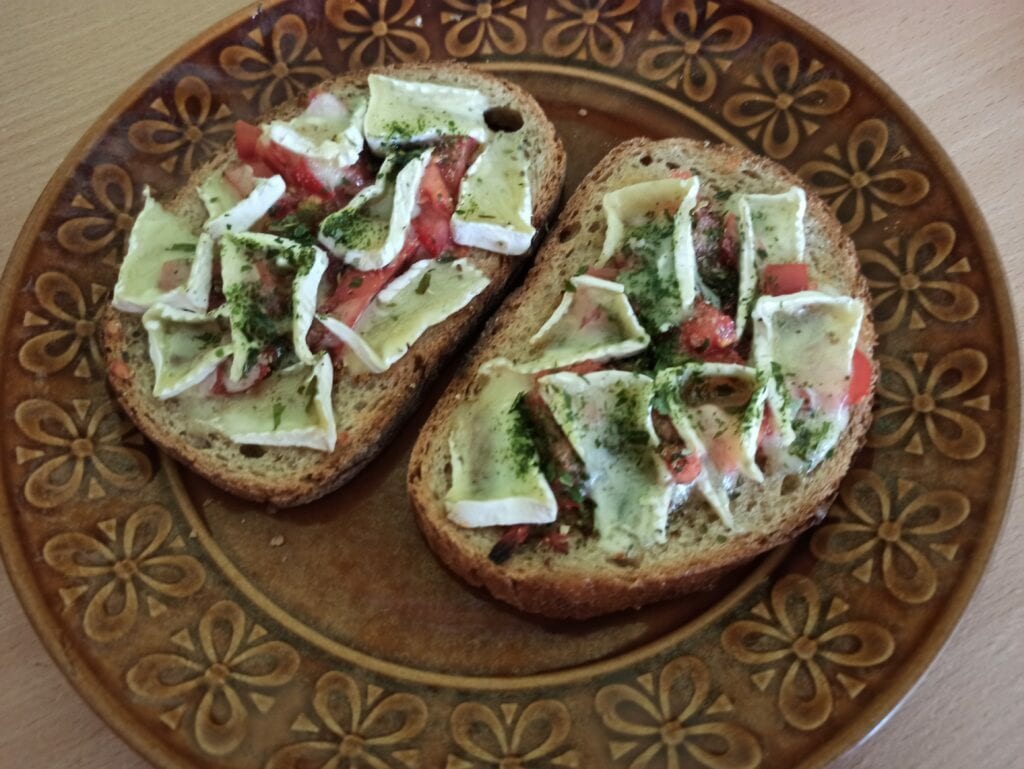 Na talerzu leżą dwie bruschetty z pomidorami i rozpuszczonym serem camembert.