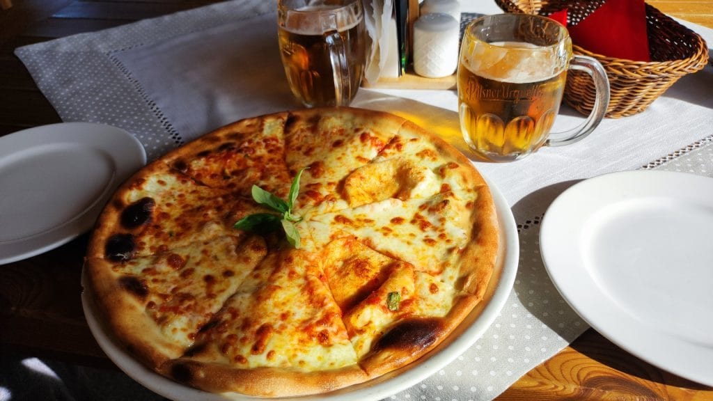 Na stole na talerzu leży cała pizza, obok dwa kufle z piwem.